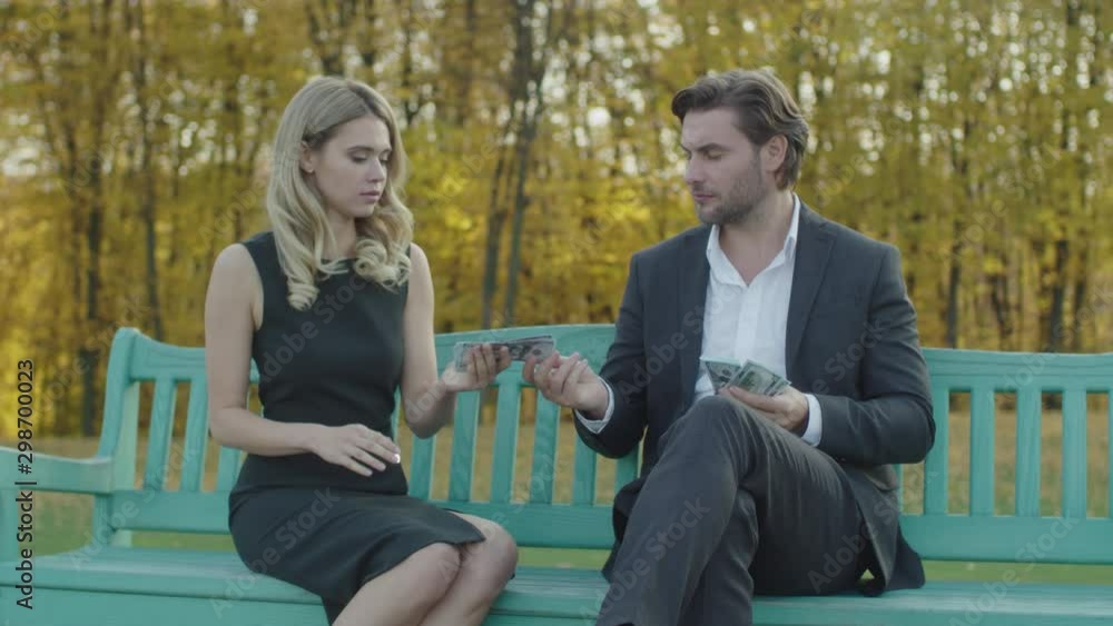 A businessman counts the money and gives part of the amount to the girl. Blonde woman counts money A businessman counts the money and gives part of the amount to the girl. Blonde woman counts money