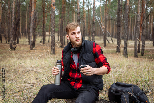 Man resting in the forest and drinking tea from the thermos.
