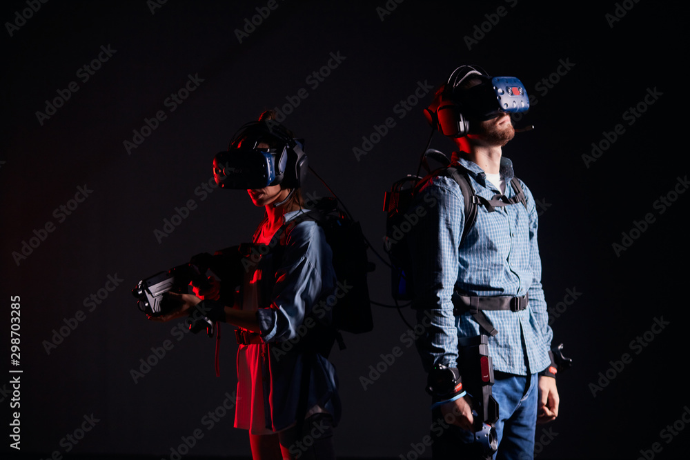 Man and woman wearing special goggles for vr futuristic games, stand back to each other. Special virtual weapons in hands. Isolated over black background Man and woman wearing special goggles for vr futuristic games, stand back to each other. Special virtual weapons in hands. Isolated over black background