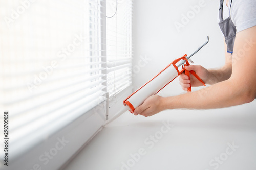 Construction worker use gun silicone tube for repairing and installing window in house photo