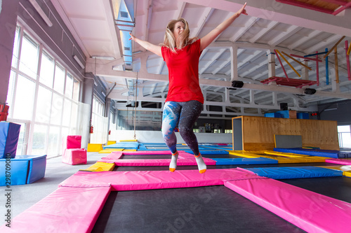 Fitness, fun, leisure and sport activity concept - Young happy woman jumping on a trampoline indoors