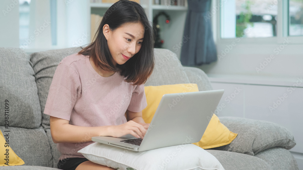 Young business freelance Asian woman working on laptop checking social media while lying on the sofa when relax in living room at home. Lifestyle latin and hispanic ethnicity women at house concept. Young business freelance Asian woman working on laptop checking social media while lying on the sofa when relax in living room at home. Lifestyle latin and hispanic ethnicity women at house concept.