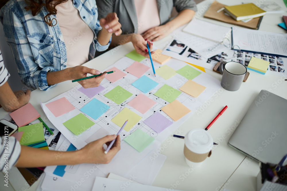 © Seventyfour - High angle view of creative team planning startup project on table, focus on hands pointing at colorful sticky notes during meeting, copy space