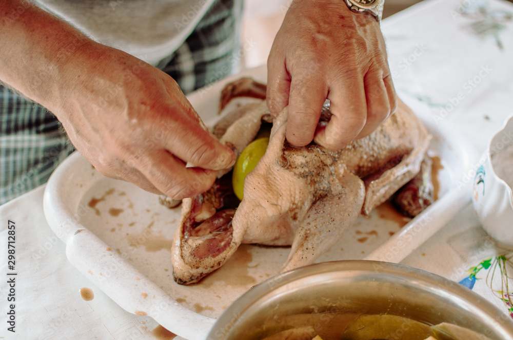 Whole duck fresh and raw on a tray with ingredients ready to cook and spices for baking. A man starts a Peking duck with apple filling. The concept of cooking recipes.
