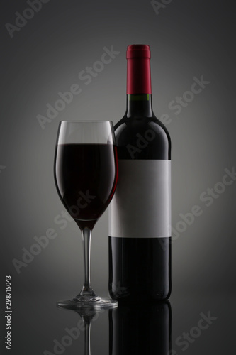 Bottle of red wine with label and wineglass on gradient background