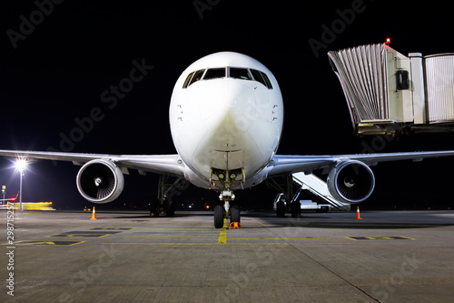 Big modern white aircraft on the parking area in the airport at night, front view