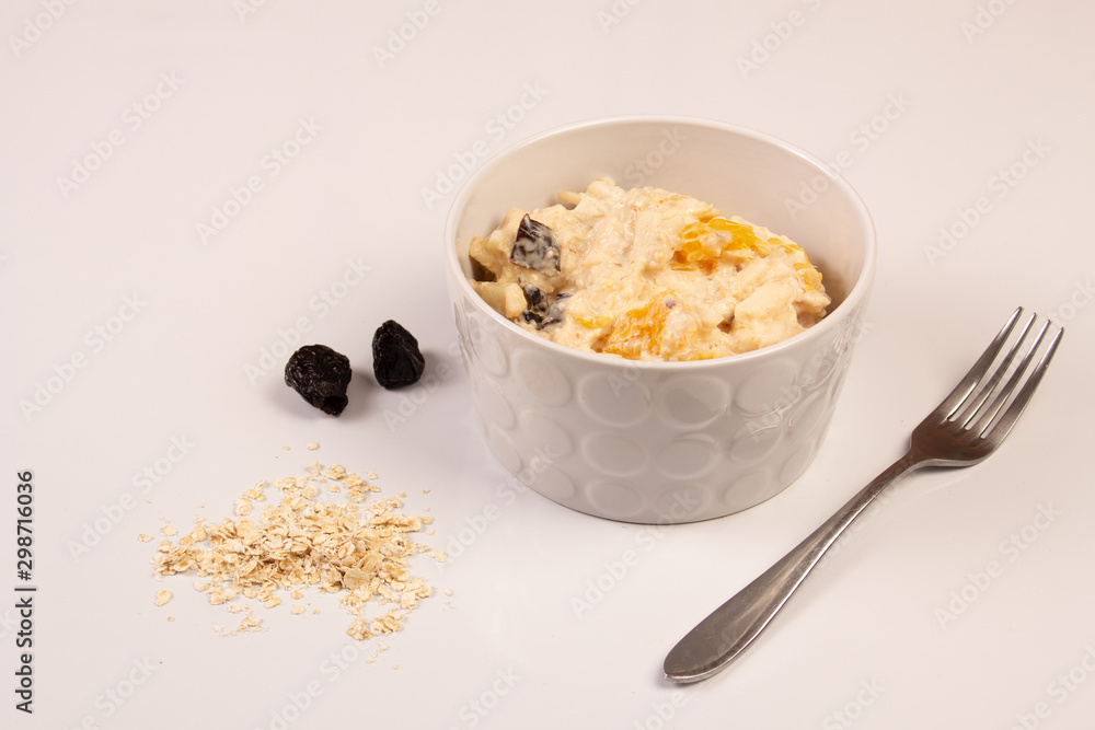 Salad of apple, orange, oat hops and prunes with honey in a white plate on a white background. Salad of apple, orange, oat hops and prunes with honey in a white plate on a white background.