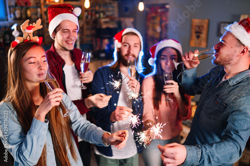 Friends celebrating new year's together. Portrait of Friends With Drinks Enjoying Cocktail Party. Young people laugh. Group of beautiful young people in Santa hats. Blur Background.