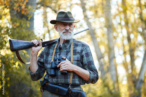 Foto Senior hunter on birds holding gun on shoulder, straighten hat, looking away