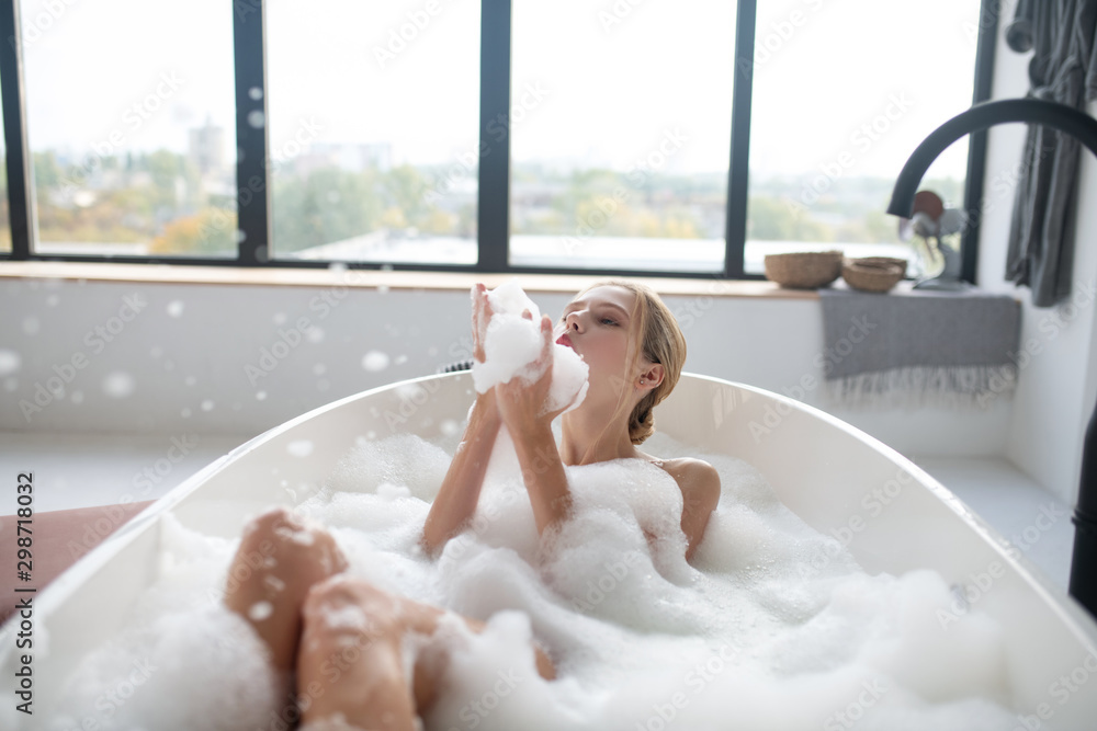 Blonde woman chilling in foamy bath having much fun - obrazy, fototapety, plakaty 