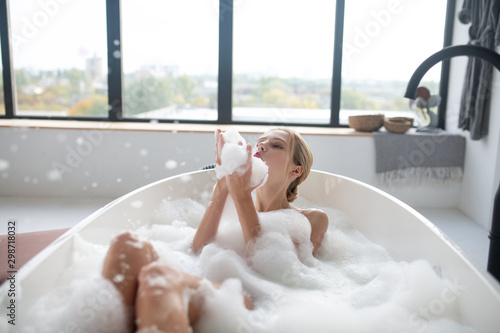Stampa su tela Blonde woman chilling in foamy bath having much fun