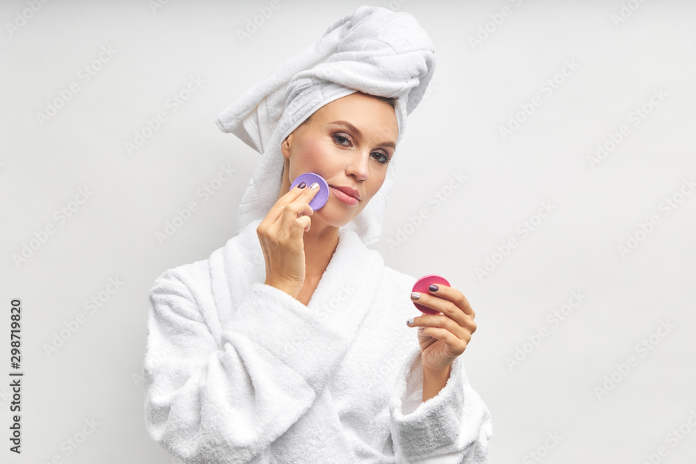 Young woman in bathrobe and towel use beauty sponges. Isolated over white background Young woman in bathrobe and towel use beauty sponges. Isolated over white background
