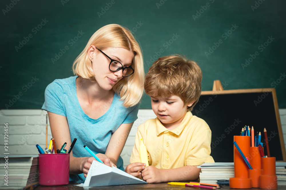 Child and teacher near chalkboard in school classroom. Teacher helping young boy with lesson. Ready for school. Elementary school. Child and teacher near chalkboard in school classroom. Teacher helping young boy with lesson. Ready for school. Elementary school.