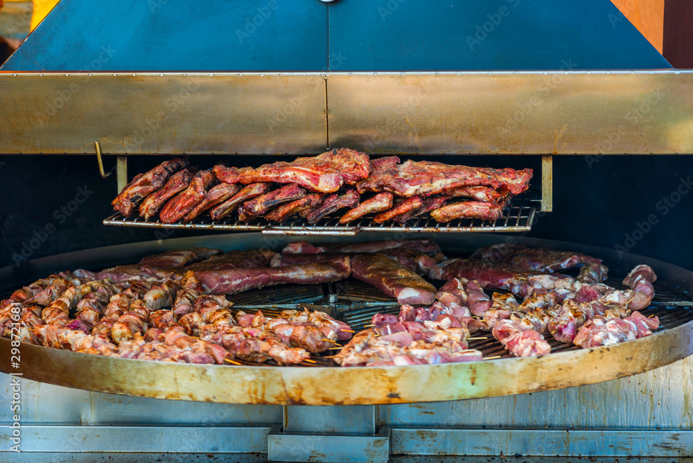 Grilled meat. Close-up cooking of large juicy pieces of raw, fat, natural, marinated pork meat, beef calves, rams on a griddle grill. A large round grill on the coals in which grilled meat