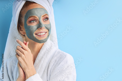 Female with perfect skin and natural make-up. Wearing bathrobe and towel after bathing, using mask. Isolated over blue background