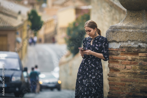 Pretty young woman in a black dress using smartphone at old town street. Travel by Europe.