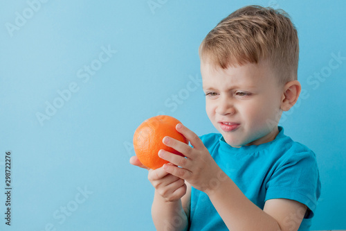 Little Boy Holding an Orange in his hands on blue background, diet and exercise for good health concept