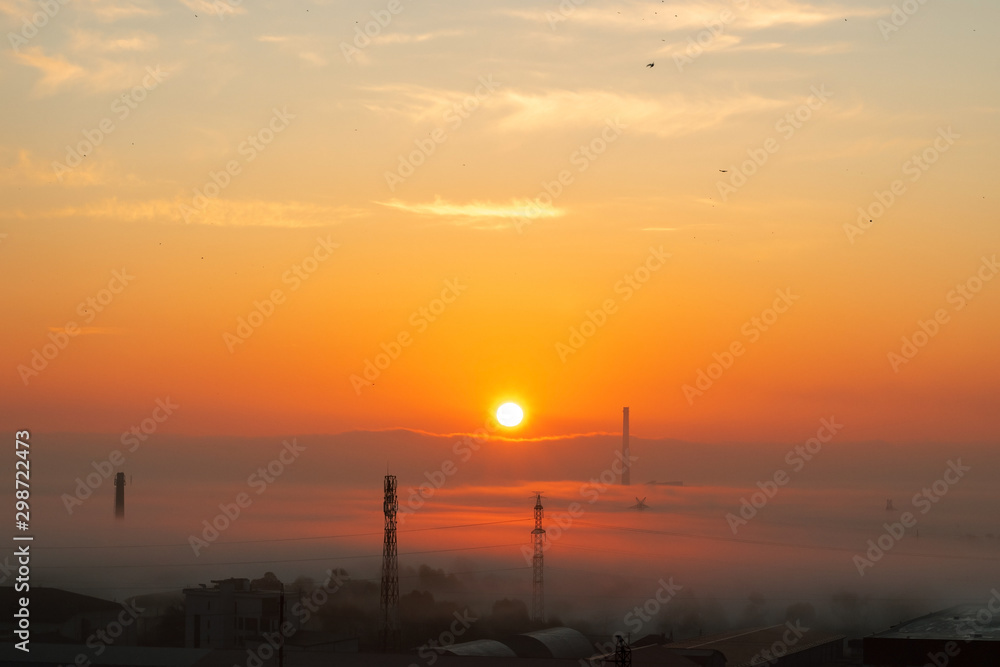 Morning misty industrial city. The Sun Has Just Risen. Power lines and factory pipes in the fog. Dark light, red purple orange sky. The beauty of industrial cities concept.