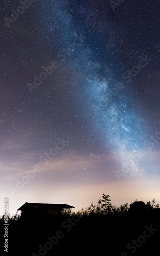 Milky Way with lonely Boathouse on the hill. Landscape with night starry sky and lonely Boathouse in the front.