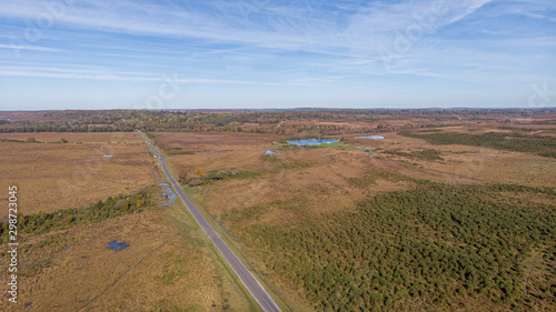 An aerial pamoramic view of the New Forest along a rural road with heartland, forest, pond and wild vegetation with beautiful autumn colors under a majestic blue sky and white clouds