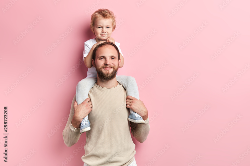 handsome little boy sitting on father's shoulders in front of pink background. close up portrait, studio shot , copy space
