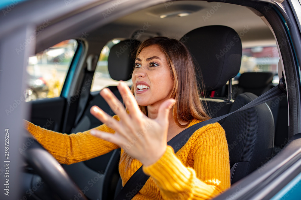 Beautiful angry woman honking in her car while driving. Angry woman driving a car. The girl with an expression of displeasure is actively gesticulating behind the wheel of the car.