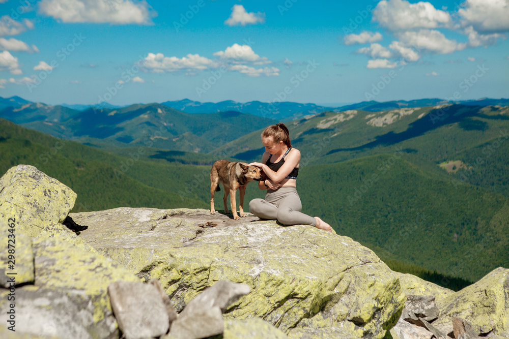 Girl with a dog on top of a mountain watching a beautiful landscape with arms wide open
