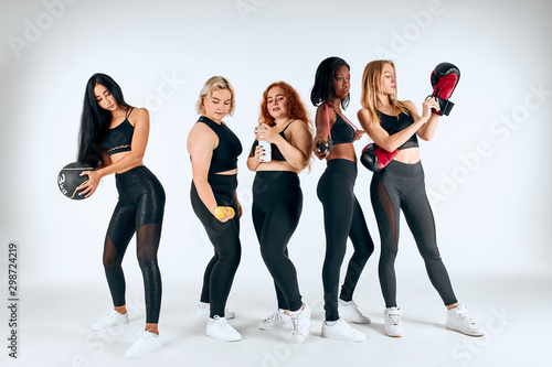 Young different girls doing sport exercises isolated over white background, using sportive things, dumbbells, boxing gloves. Different sizes, hair colors, races. Healthy lifestyle, sport concept