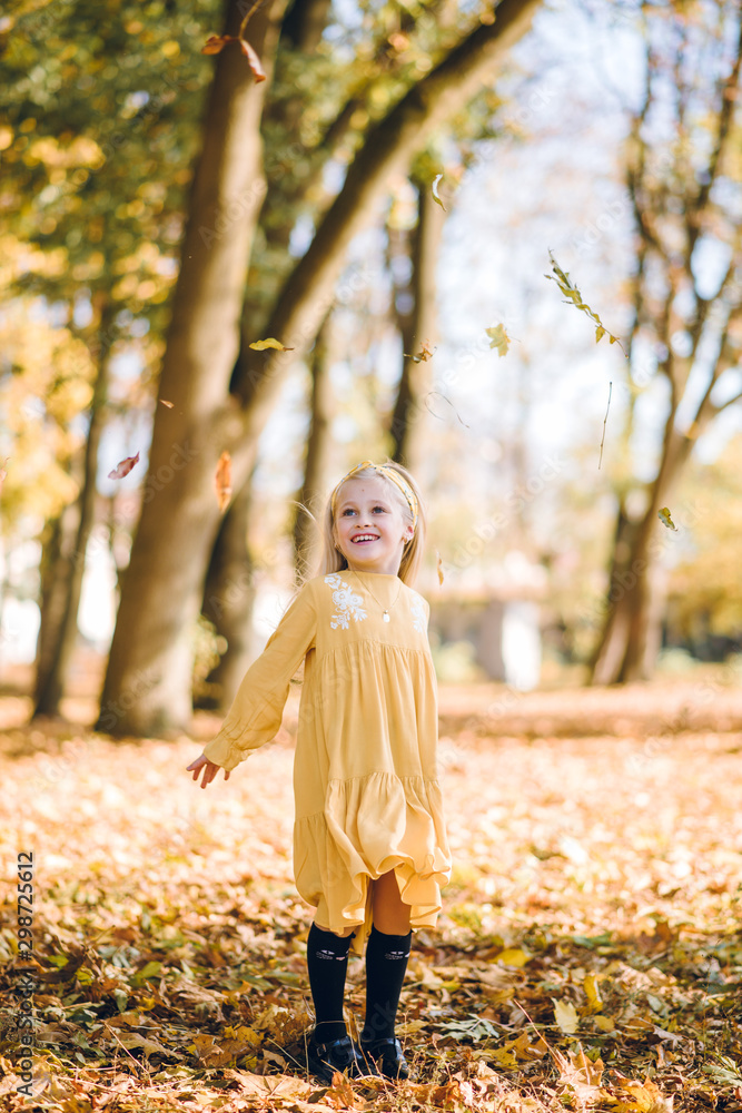 beautiful little girl with blond hair in a yellow dress having fun playing in autumn park beautiful little girl with blond hair in a yellow dress having fun playing in autumn park