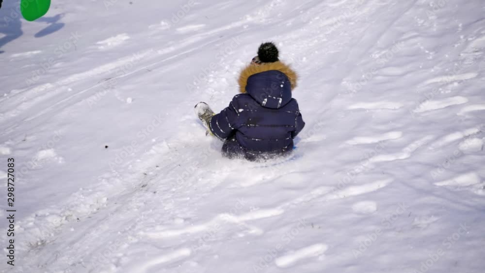 Boy on a snow slides. Little child sledding on plastic sled happily from the white hill in winter. Slow motion. Boy on a snow slides. Little child sledding on plastic sled happily from the white hill in winter. Slow motion.