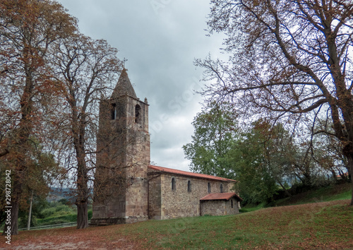  Autumn trees with brown leaves and ground covered by leaves  in the park with old church. North of Spain.
