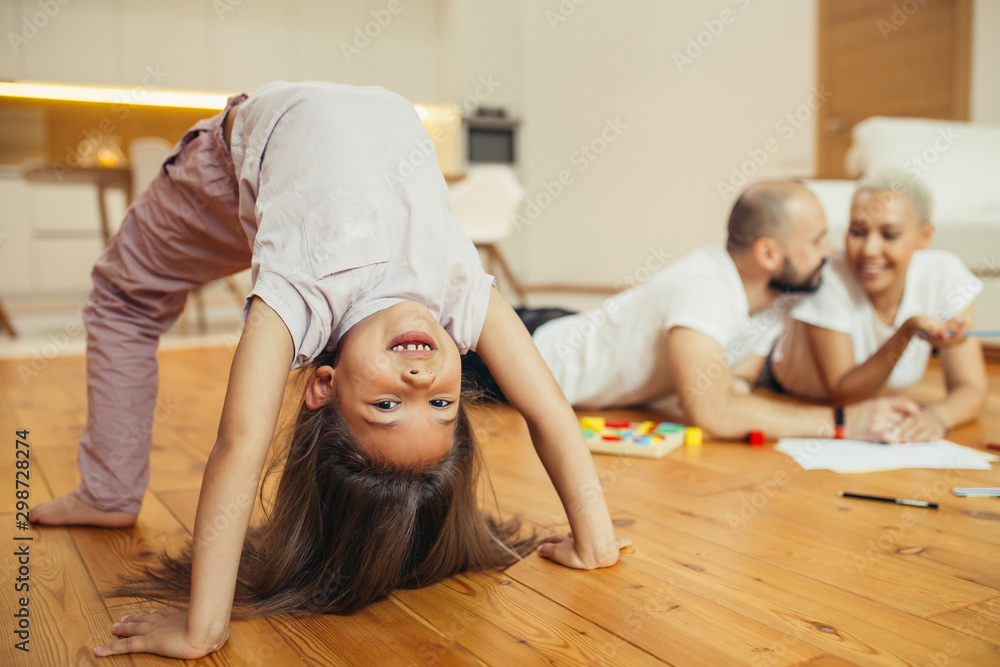 Daughter performing bridge at home. Parents ltying on floor. Happy family, love concept