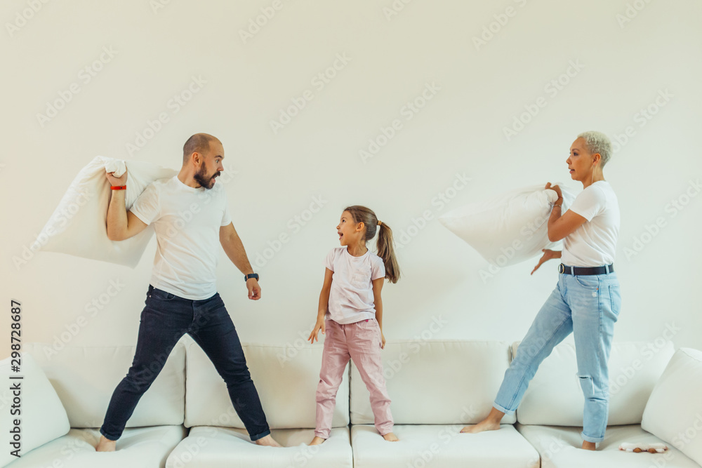 Obraz premium Happy joyful family fighting pillow battle on bed at home with children. Parents have pillow fight with daughter. Positive family, laughing. Friendly family