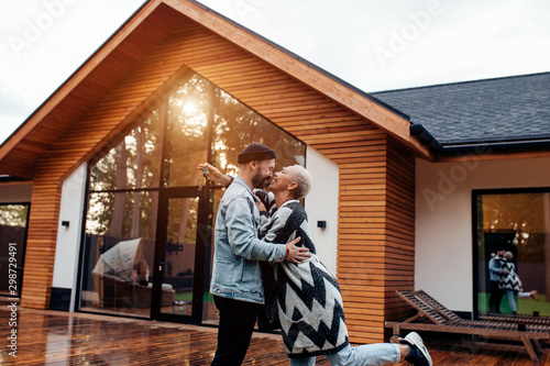 Male and female in casual clothes kissing next to countryhouse. Happy to spend free time together in new house. Love, relationships concept