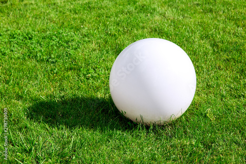 Ball ground lamp, white round shade lantern on green grass with copy space on a sunny summer day.