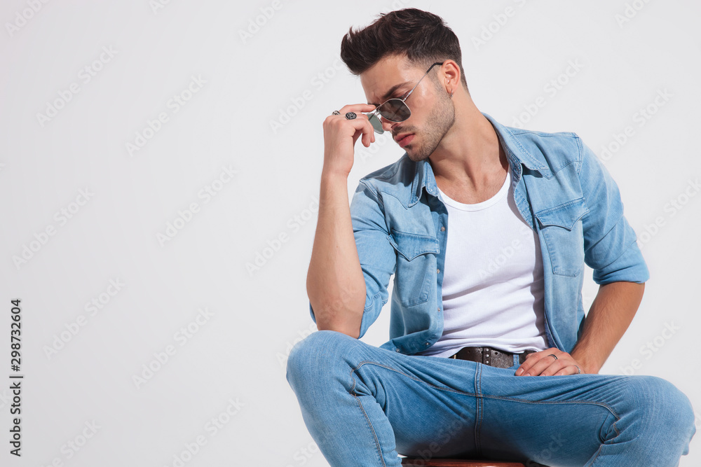 Thoughtful casual man looking down and fixing his sunglasses Thoughtful casual man looking down and fixing his sunglasses