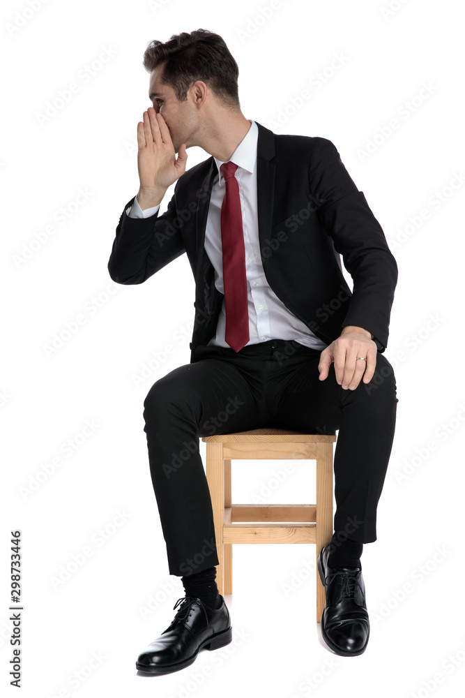 Young businessman holding his hand over his mouth and gossiping