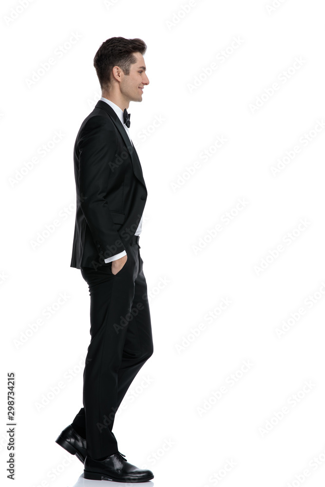 side view of smiling young groom in tuxedo walking side view of smiling young groom in tuxedo walking