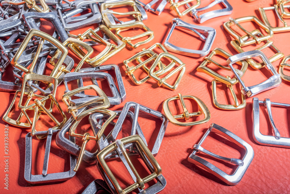 A lot of metal buckles for belts on red genuine full grain leather. Leather workshop A lot of metal buckles for belts on red genuine full grain leather. Leather workshop