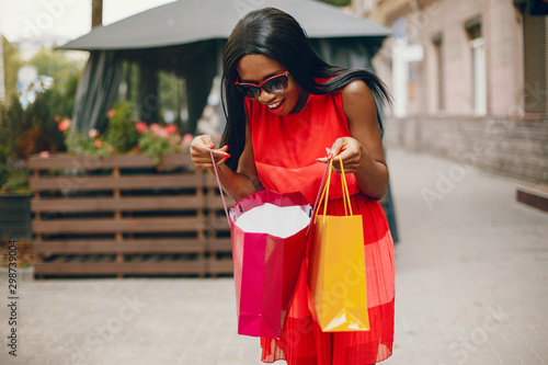 Black girl in a summer city. Woman with a shoping bags. Lady in a red ress