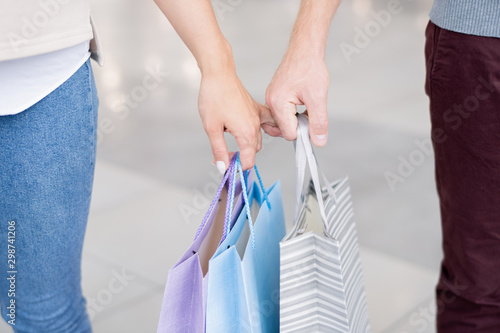 Hands of young affectionate couple carrying paperbags and holding by fingers