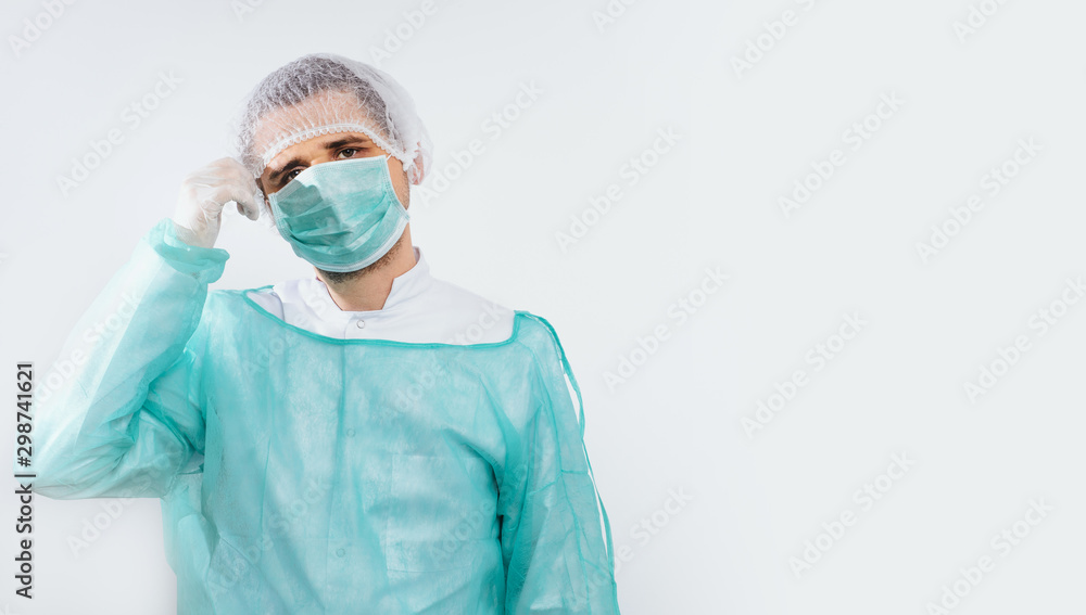 Preparing for surgery, dressing the surgeon. A man wearing a green surgical apron and a face mask on a light background. Medical and pharmaceutical concept. Saving lives. Preparing for surgery, dressing the surgeon. A man wearing a green surgical apron and a face mask on a light background. Medical and pharmaceutical concept. Saving lives.
