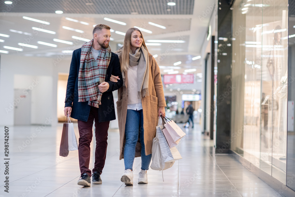 Fototapeta premium Young casual couple with paperbags looking at clothes in shop window