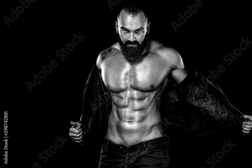 Men's fashion concept. Close-up portrait of a brutal bearded man topless in a leather jacket. Athlete bodybuilder on black background.