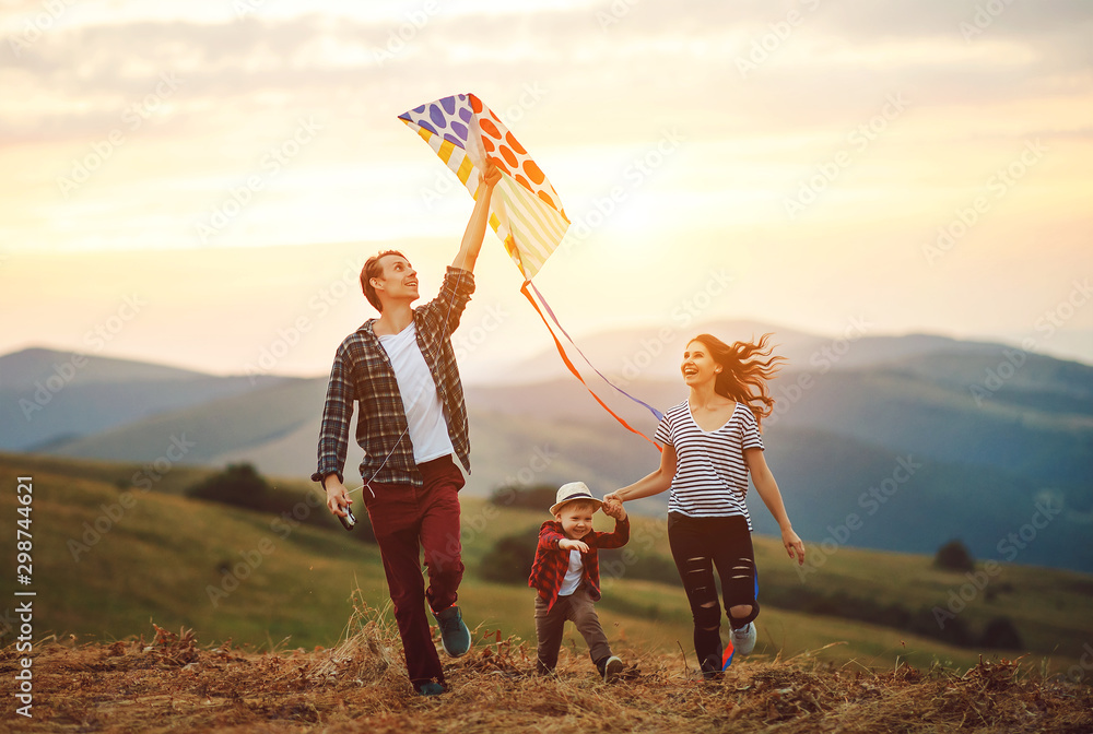 Happy family father of mother and child son launch a kite on nature at sunset. - obrazy, fototapety, plakaty 