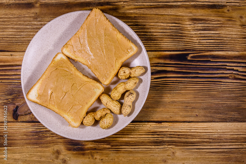 Glass jar with peanut butter and plate with sandwiches on a wooden table. Top view Glass jar with peanut butter and plate with sandwiches on a wooden table. Top view