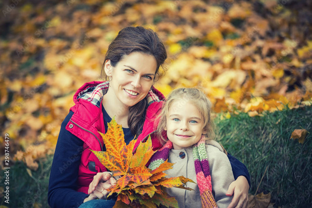 Smiling little girl and her mother enjoy walk in autumn park and play with bright autumn leaves Smiling little girl and her mother enjoy walk in autumn park and play with bright autumn leaves