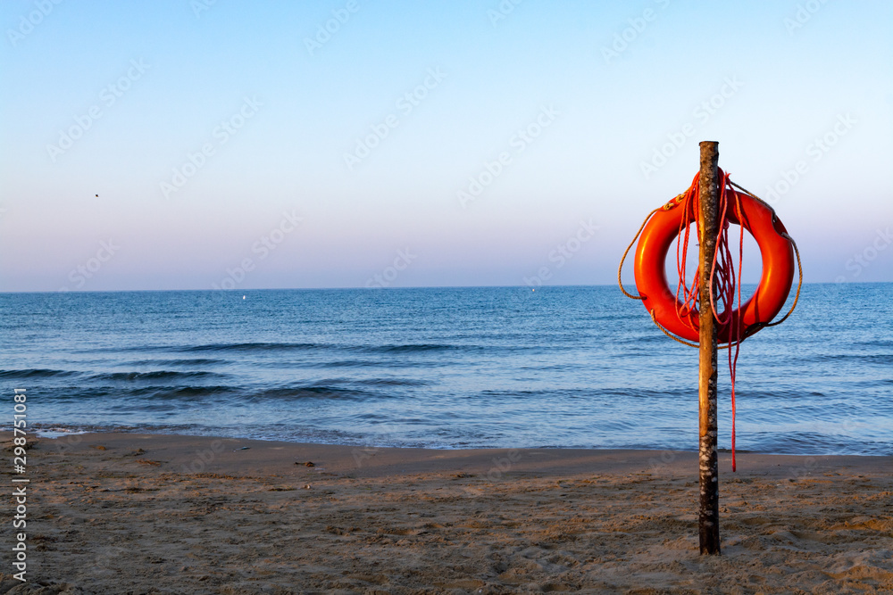 Red lifebuoy with rope on sandy beach, life save in sea water concept
