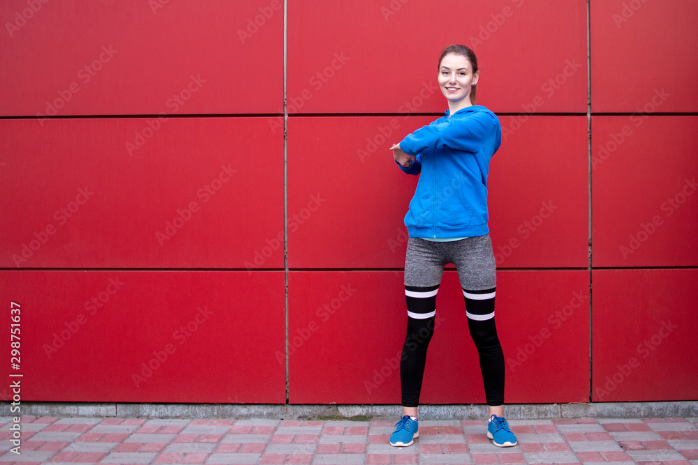 sporty girl is training against a red wall in the street, a woman is doing warm-up in sportswear outdoors, copy space