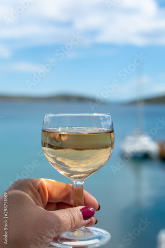 hand with glass of white wine served outside on balcony with sea view